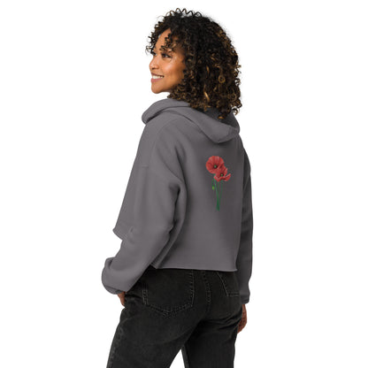 Seiten- und Rückenansicht eines Models mit braunen Locken, die den grauen Cropped Hoodie von POLCOUTURE trägt. Das Model blickt über die Schulter zur Seite, wodurch der minimalistische Mohnblumen-Print auf dem Rücken sowie der lockere, bauchfreie Schnitt des Hoodies perfekt zur Geltung kommen.