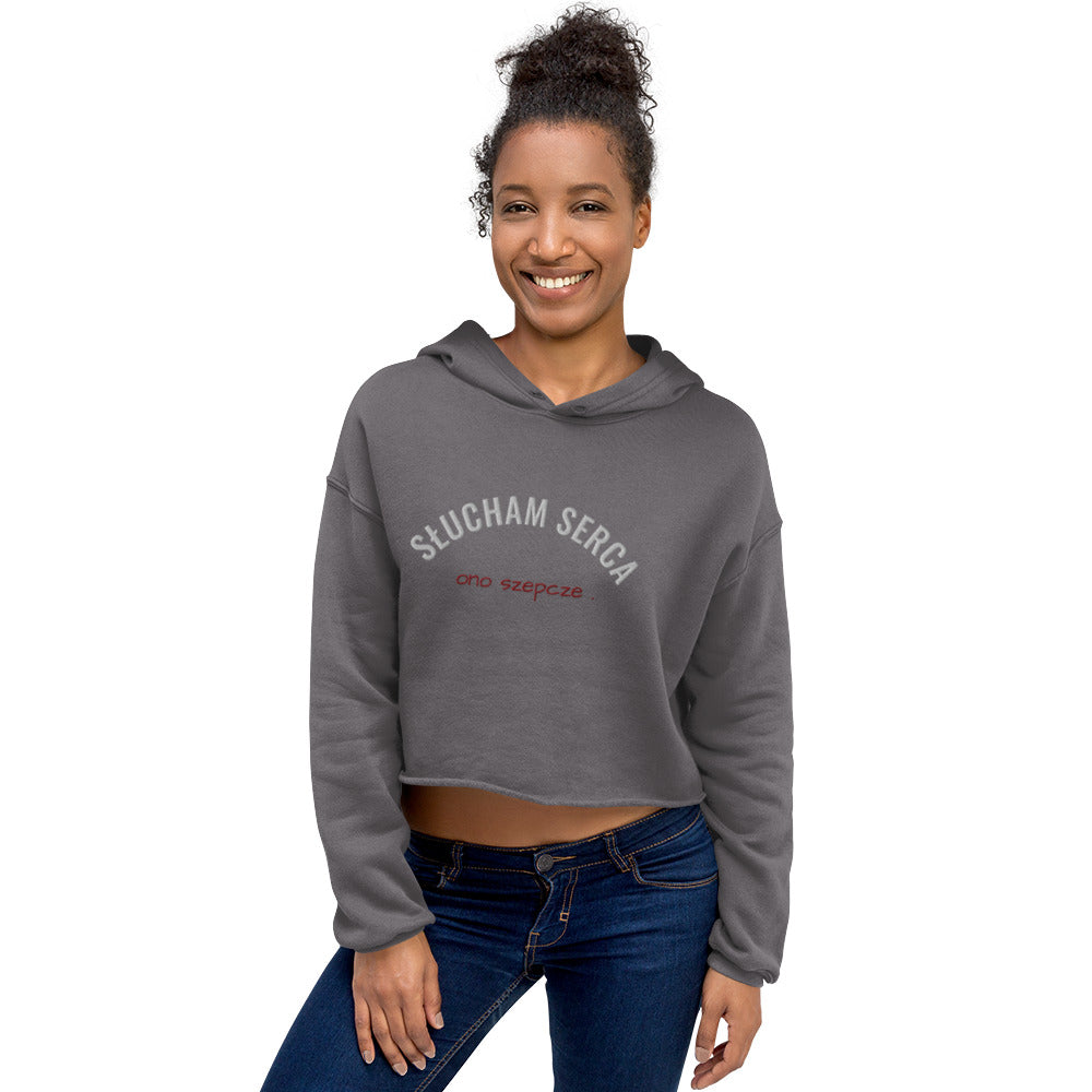 Ein Model mit dem grauen Cropped Hoodies von POLCOUTURE. Auf der Vorderseite befindet sich eine hochwertige Stickerei: Der Schriftzug „słucham serca“ in Weiß und direkt darunter „ono szepcze“ in rot.