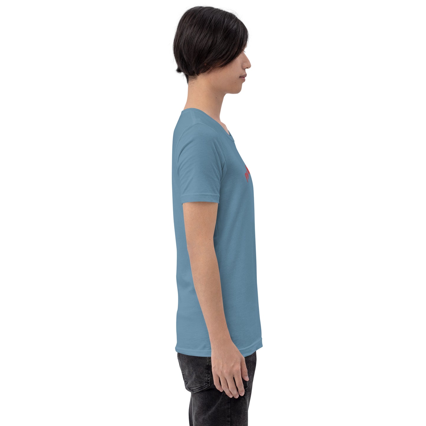 Seitenprofil eines Models in einem stahlblauen POLCOUTURE Unisex-T-Shirt. Auf der Brust ist der Teil des Drucks „Pan“ in roter Schrift zu sehen. Die Ansicht zeigt den hochwertigen Stoff in Steel Blue.