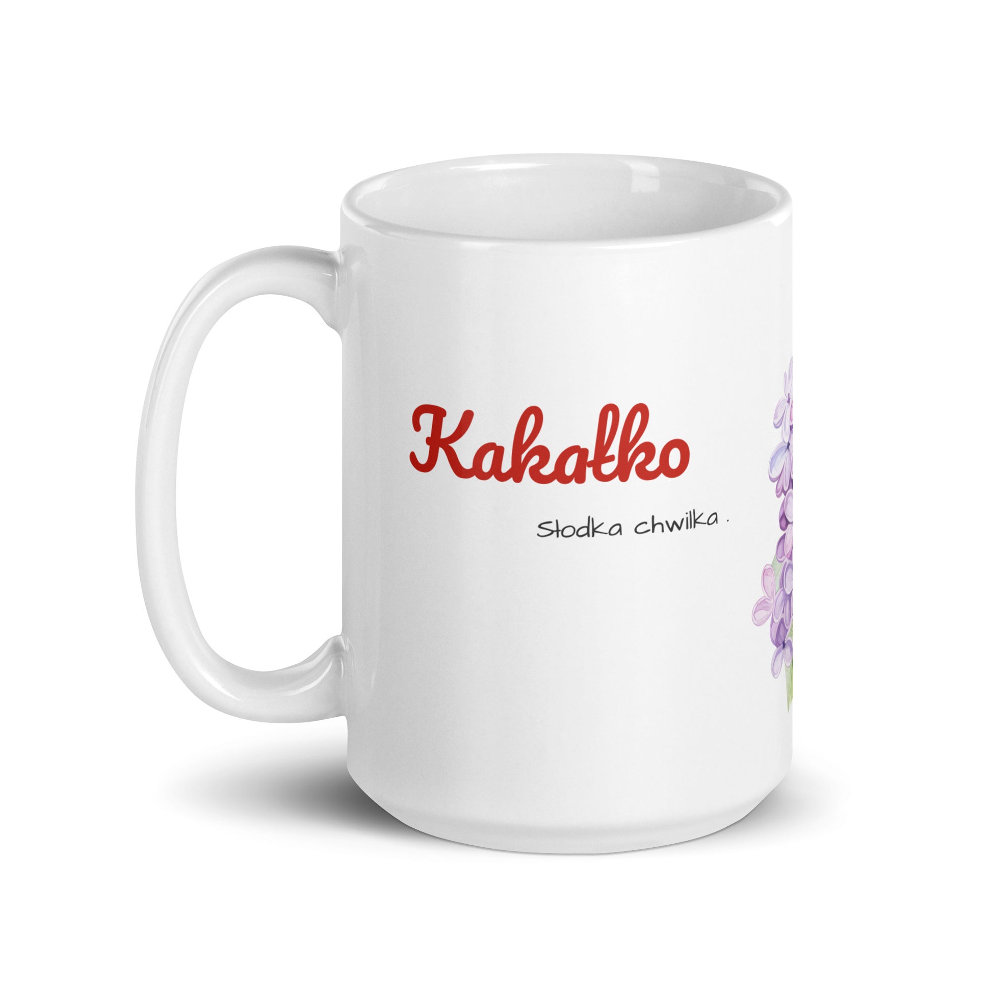 Seitenansicht der weißen POLCOUTURE Tasse mit Henkel links. Im Fokus steht das polnische Wort „Kakałko“, mit dem Slogan „słodka chwilka“ klein direkt darunter. Die fliederfarbenen Blüten sind bei dieser Ansicht kaum zu sehen.