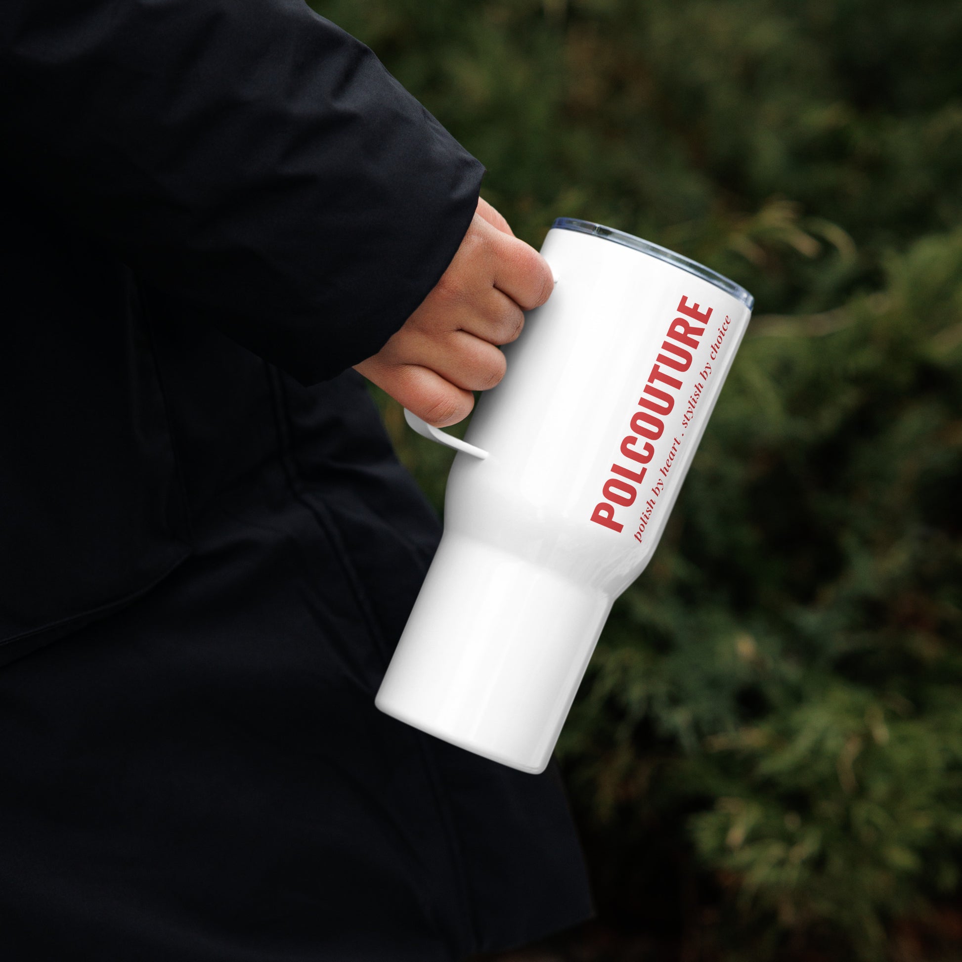 Person in schwarzem Hoodie hält den weißen Travel Mug „ŁYK“ von POLCOUTURE in der rechten Hand. Der Schriftzug POLCOUTURE ist erkennbar.