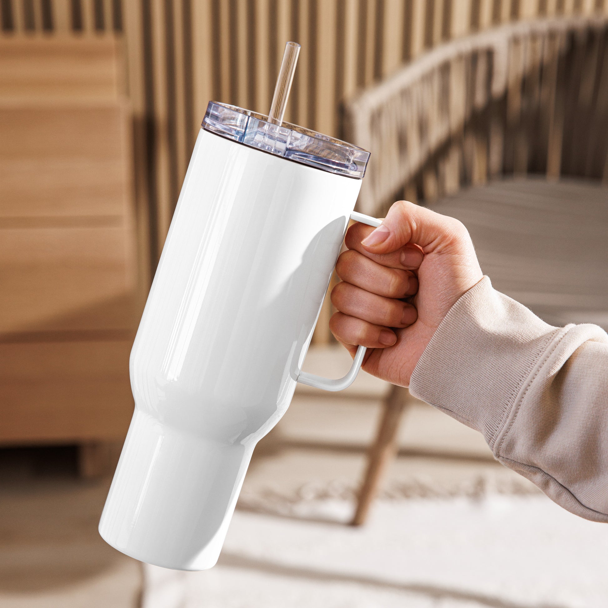 Rückseite des weißen Travel Mug „ŁYK“ von POLCOUTURE in der rechten Hand. Die glatte, weiße Edelstahlfläche steht im Kontrast zum hellen Pulli und einem sanft verschwommenen Hintergrund. Das minimalistische Design fügt sich perfekt in einen modernen Alltag ein.