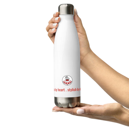 Frontalansicht der Trinkflasche „KROPELKA“ von POLCOUTURE auf weißem Hintergrund. Die rechte Hand hält die Flasche oben, während die linke Hand sie von unten unterstützt. Das Logo und der Slogan sind mittig zu sehen.